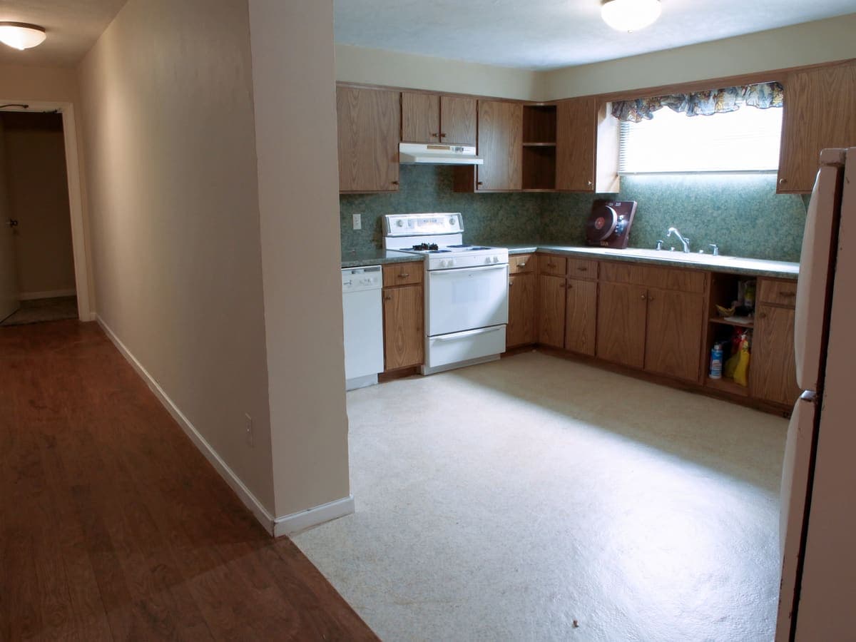 Kitchen with original wood-veneer cabinets, worn linoleum flooring, and older appliances