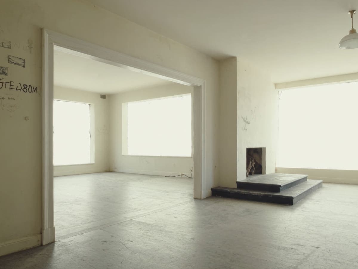 Bare, dusty interior of a vacant house with one window boarded over
