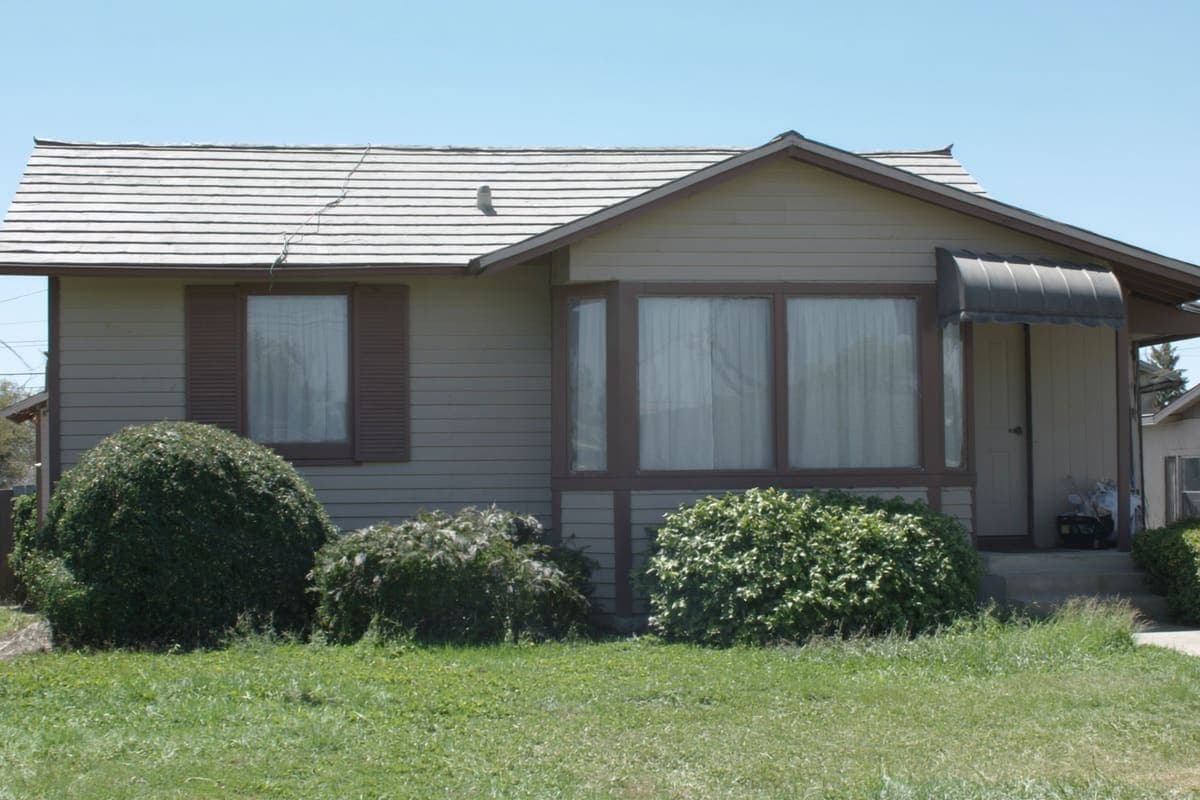 Closed-up single-family house with drawn curtains and an overgrown front yard
